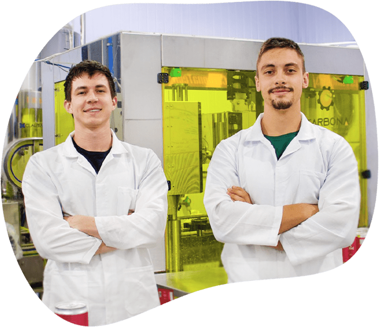 Vinícius e Leonardo, fundadores da Pod, de jaleco branco na frente da máquina de envase da fábrica